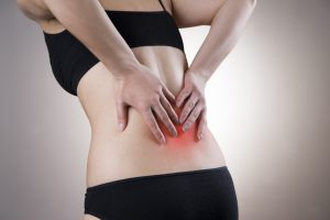 Pain in back of women on gray background. Caring for the female body. Red dot