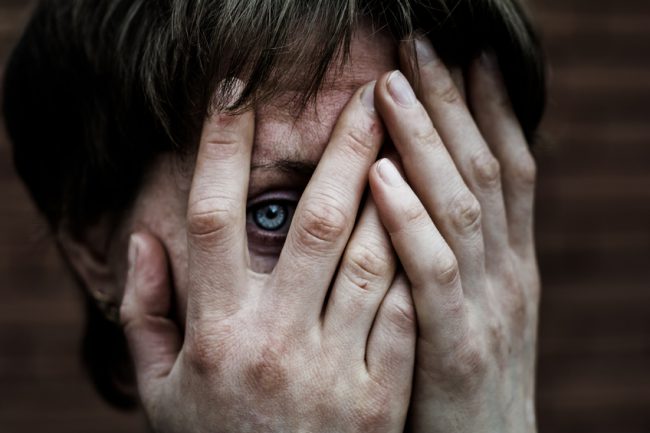 A woman in a very depressed mood covers his face, near a brick wall.