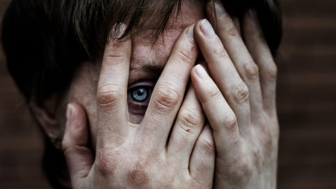 A woman in a very depressed mood covers his face, near a brick wall.